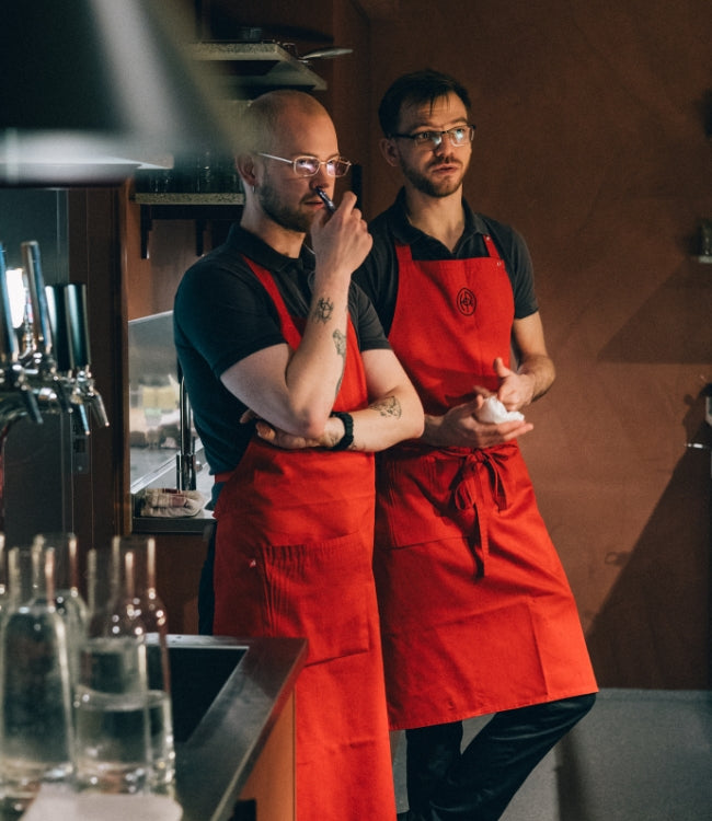 Två kockar i röda förkläden står i restaurang och samtalar inför julbord – varm stämning och teamwork.