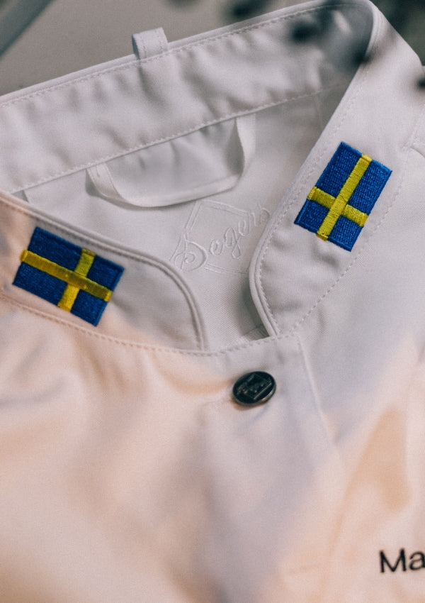 Närbild på vit kockrock med broderad flagga på kockrockens krage.