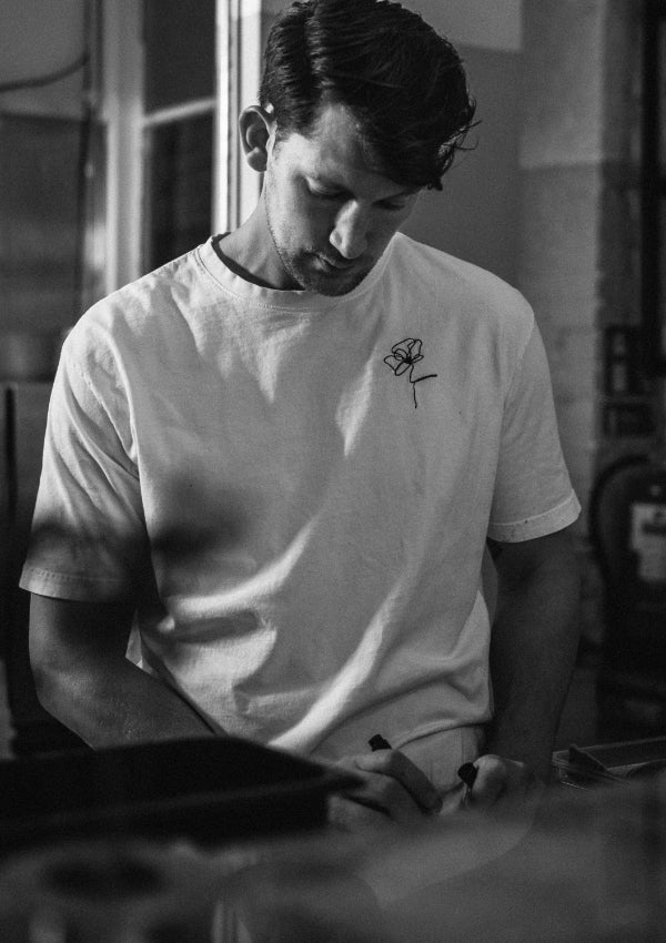 Kock i vit t-shirt med broderad blomma arbetar koncentrerat i kök, svartvit bild.