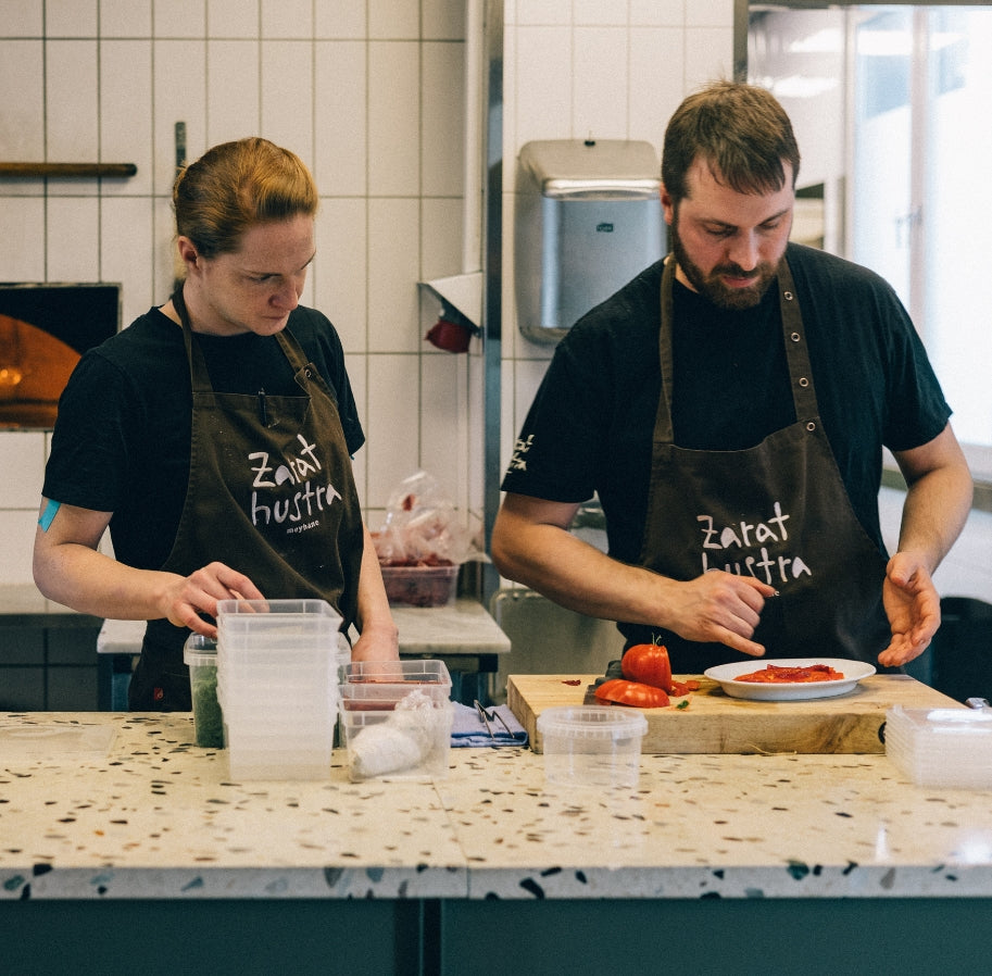 Två kockar med gröna förkläden förbereder mat tillsammans i restaurangkök.