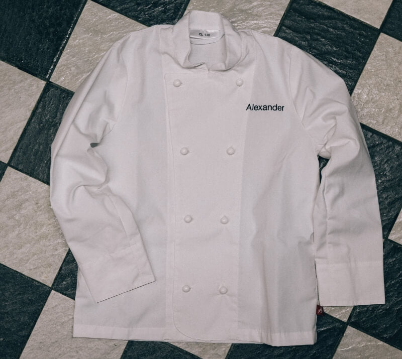 Vit kockrock i barnstorlek med namnet Alexander broderat på bröstet. Personlig brodyr på kockkläder för barn.